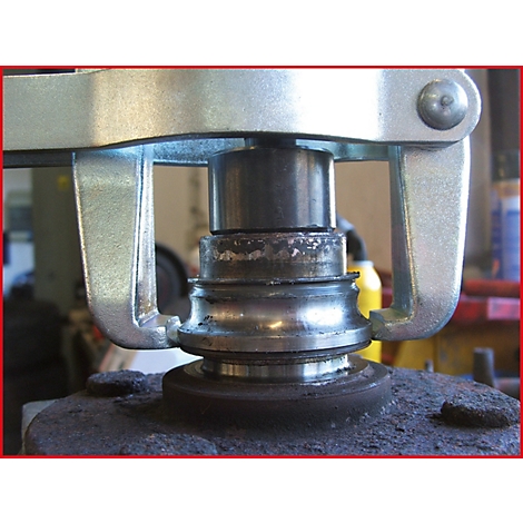 Nahaufnahme einer metallenen Vorrichtung, die ein Lager ausbaut. Die Werkzeugarme umgreifen die Bestandteile.